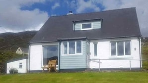 Ein zweistöckiges Haus mit dunklem Dach, weißen Wänden und einem kleinen Fenster im Obergeschoss.