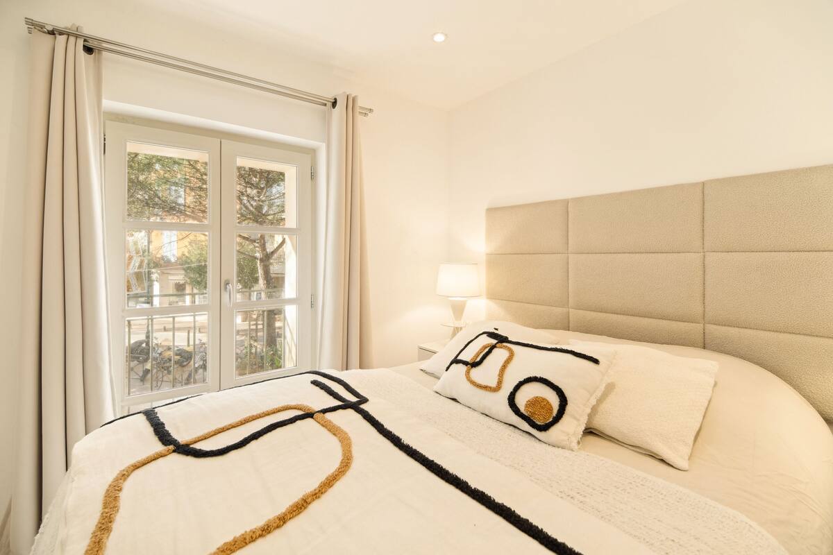 Une chambre avec un grand lit, une fenêtre avec des rideaux, une lampe de chevet et une vue sur l’extérieur.