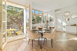 A dining area with a glass table, four chairs, and a view of trees through large windows. - Résidence Celli Saint-Tropez (Saint-Tropez)