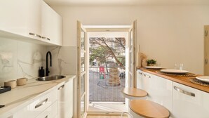 Una cocina moderna con armarios blancos, un protector contra salpicaduras de mármol y vistas al exterior a través de una puerta abierta.