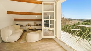 Una sala de estar moderna con un sofá, un reposapiés y un ventanal de vidrio que da a un balcón con mobiliario exterior.