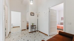 Una habitación con un sofá marrón, una lámpara de pie, una mesita con una planta y una cama con edredón estampado.