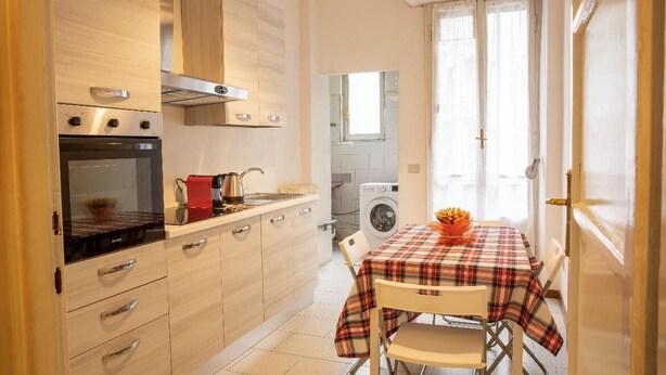 Cocina compacta con horno empotrado, cafetera y lavadora al fondo.