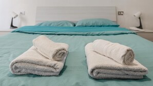 Una cama bien hecha con ropa de cama color aguamarina y dos toallas blancas enrolladas al pie.