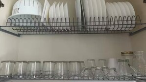 Una cocina con un estante metálico que contiene platos y tazones, y un estante inferior con frascos de vidrio transparente.