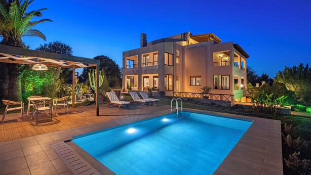 Una casa moderna de dos pisos con piscina, mobiliario exterior y una pérgola.