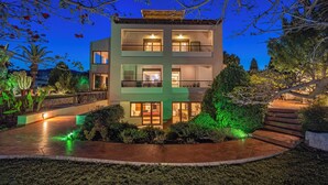Un moderno edificio de dos plantas con balcón, rodeado de jardines ajardinados y senderos iluminados.