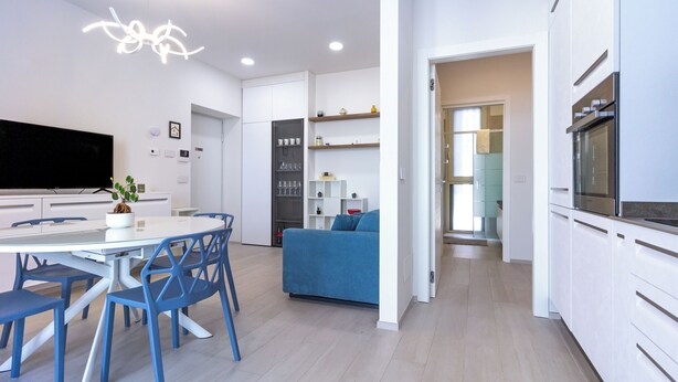 A modern kitchen with white cabinets, a built-in oven, and a dining area with a white table and blue chairs.