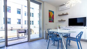 A modern kitchen with a white countertop, blue chairs, and a large flat-screen TV.