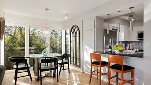 A modern kitchen with white cabinets, a black countertop, and a dining area with a glass table and black chairs. - Elegant Condo in Exclusive Polo Field Complex with Desk & Fireplace! (Carpinteria)