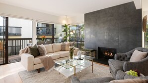 A modern living room with a glass coffee table, a beige sofa, a grey armchair, and a fireplace. - Elegant Condo in Exclusive Polo Field Complex with Desk & Fireplace! (Carpinteria)