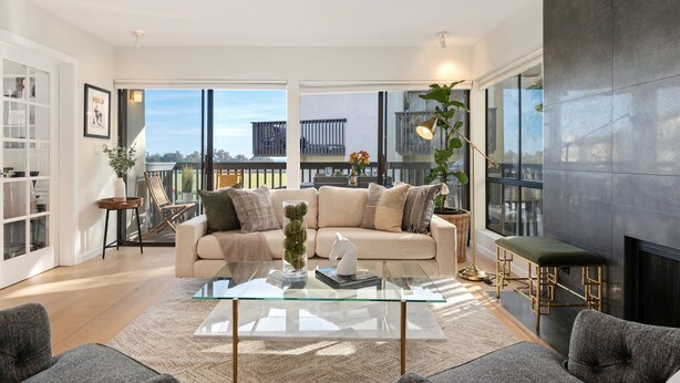 A modern living room with a glass coffee table, beige sofa, and a view of the city through large windows. - Elegant Condo in Exclusive Polo Field Complex with Desk & Fireplace! (Carpinteria)