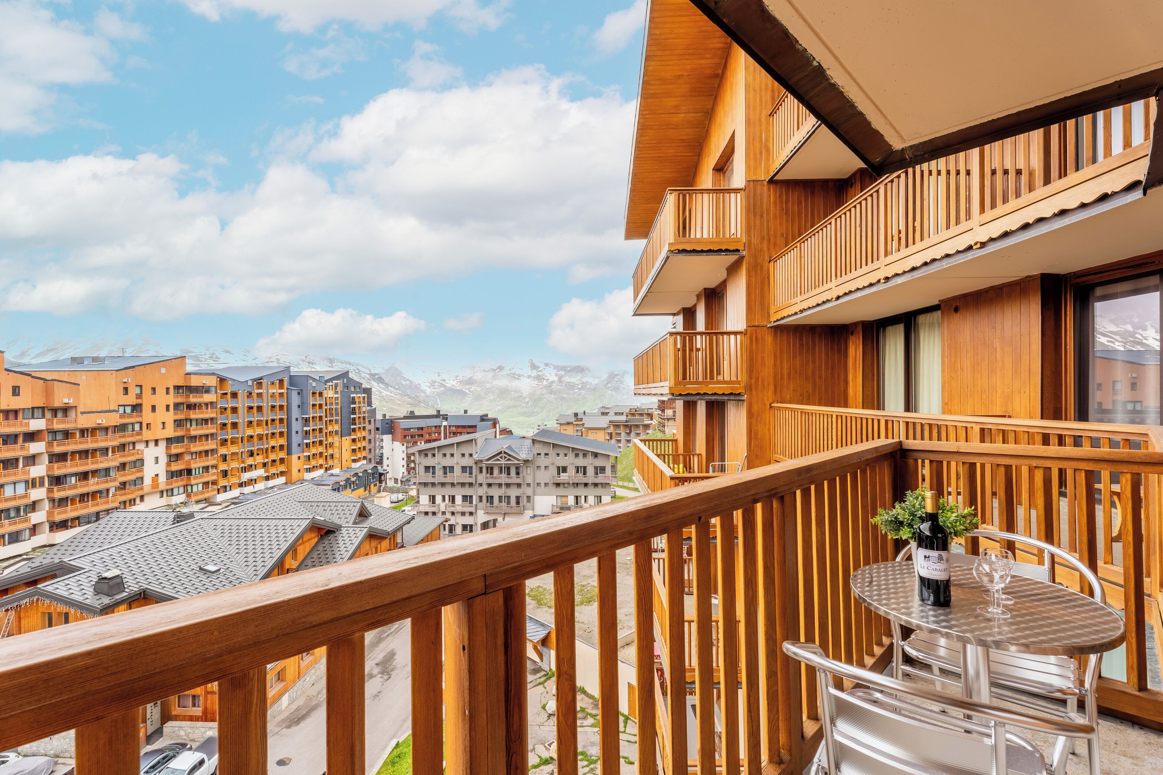 Ein Balkon mit Holzgeländer, einem Tisch und einer Weinflasche.