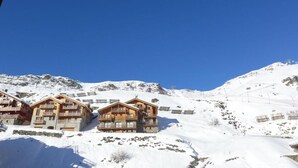 Un gruppo di chalet in legno su un pendio montuoso innevato, con cielo azzurro.