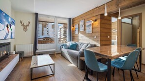 Un soggiorno moderno con soffitto in legno, un caminetto, un divano, un tavolo da pranzo con sedie e vista su una montagna tramite una porta vetrata.