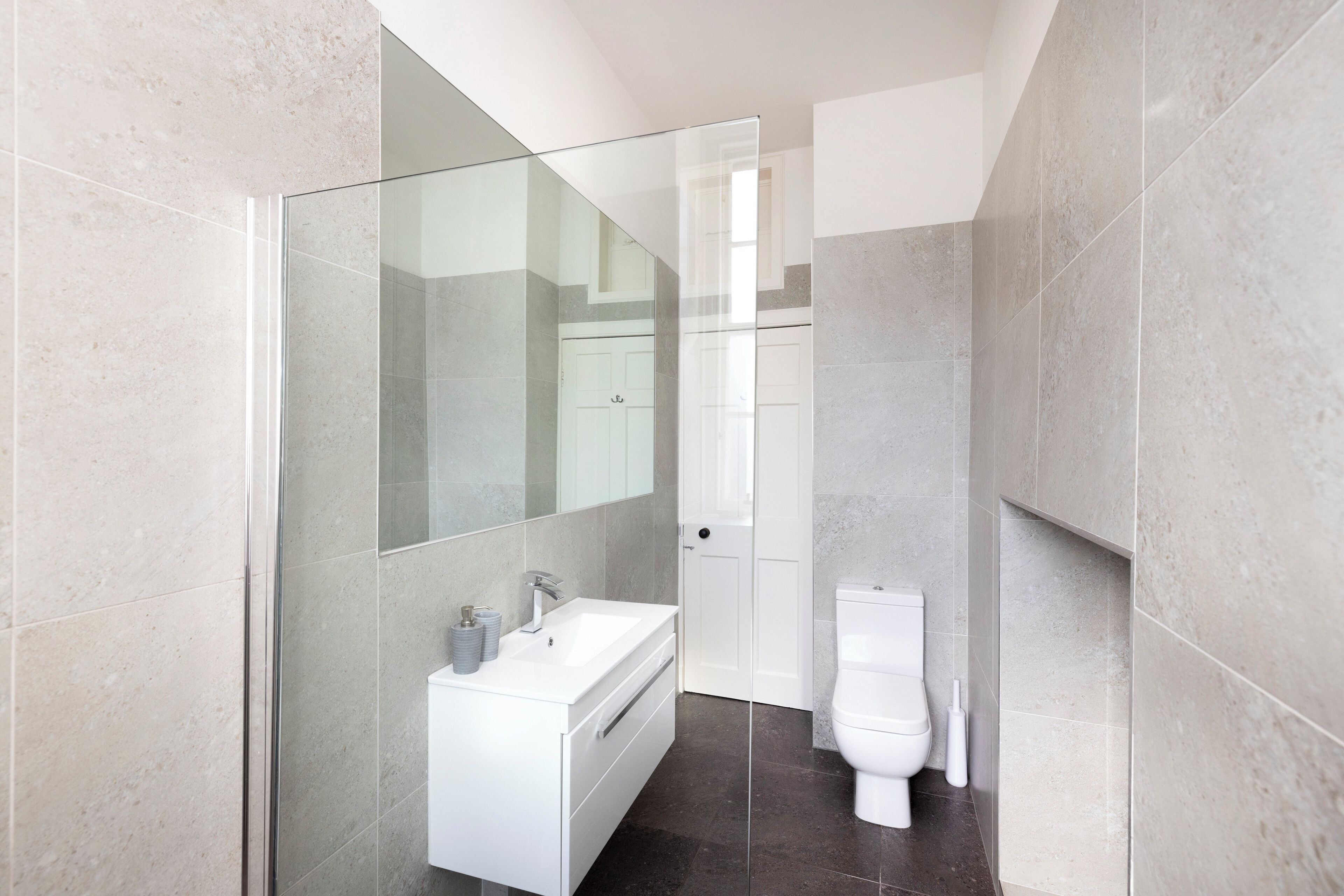 Un baño moderno con cabina de ducha de vidrio, lavamanos blanco y retrete.