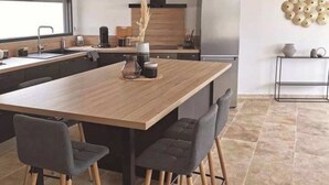 Een moderne keuken met een centraal eiland, donkere stoelen en een betegelde vloer.