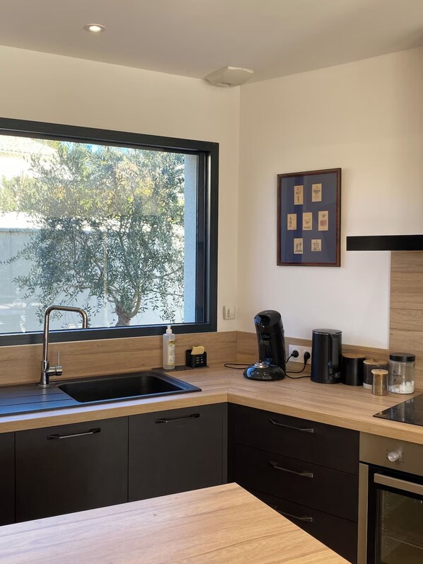 A modern kitchen with a large window, a sink, a coffee machine, and a framed artwork on the wall.