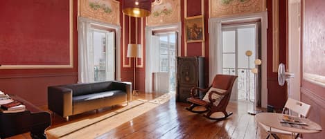 A room with a wooden floor, a sofa, a rocking chair, a table, and a cabinet.