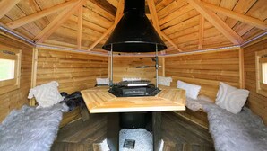 Uma cabana de madeira com lareira central, paredes de madeira e teto inclinado.