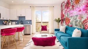 A modern living room with a blue sofa, a white coffee table, and a kitchen area with white cabinets and a blue backsplash. - The WildFlower condo in Music City near downtown (Nashville)