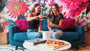 Two people sitting on a blue sofa with a floral wall mural, a book, and a plate of food on a table. - The WildFlower condo in Music City near downtown (Nashville)