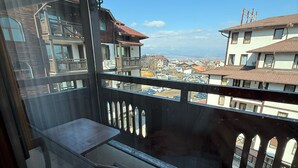 Un balcone con ringhiera in vetro, una lampada a sospensione e vista su edifici e un paesaggio lontano.