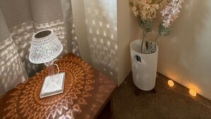 Una stanza con una panca di legno, un tavolino con una lampada, un vaso con fiori e un muro con un motivo decorativo in ombra.