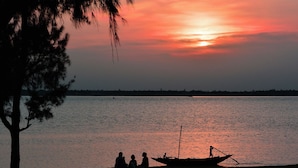 A sunset over a calm body of water with a boat and people on the shore. - Riverdale Homestay, Diamond Harbour -WB Govt Reg Gold Category (Diamond Harbour)