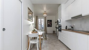 Een moderne keuken met witte kasten, een houten aanrecht en een eethoek met witte stoelen en een tafel.