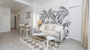 Een moderne woonkamer met een bank, salontafel en stoelen. Op de muur is een groot kunstwerk met palmbladeren te zien.