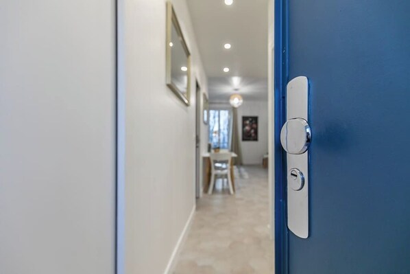 Un couloir avec une porte bleue, un mur blanc et un sol carrelé.