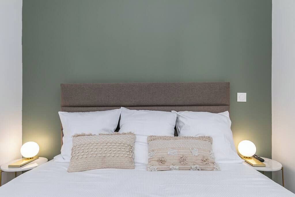 A neatly made bed with white bedding and two decorative pillows, flanked by bedside tables with lamps.