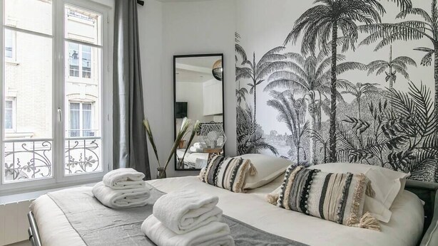 Un dormitorio con una cama grande, vistas al exterior y un mural tropical en la pared.