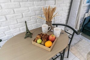 A round table with a tray of croissants, fruits, and a small Eiffel Tower model. There are two white mugs and a wicker basket with dried plants.
