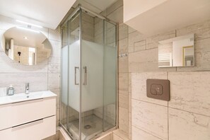 A modern bathroom with a glass-enclosed shower, a white vanity with a mirror, and a marble-tiled wall.