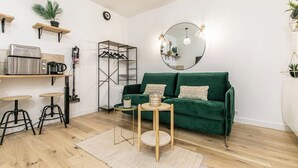 A compact living space with a green sofa, a round mirror, a small round table, and a kitchenette area with a coffee machine and a fridge. - Splendide Appart 2P- Popincourt Paris centre (Paris)