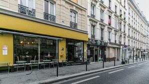 A street view with a yellow building, outdoor seating, and a pedestrian crossing. - Splendide Appart 2P- Popincourt Paris centre (Paris)