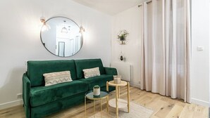 A living room with a green sofa, a round mirror, and two small tables. - Splendide Appart 2P- Popincourt Paris centre (Paris)