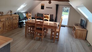 A cozy attic room with a wooden dining table, chairs, and a TV on a wooden stand.
