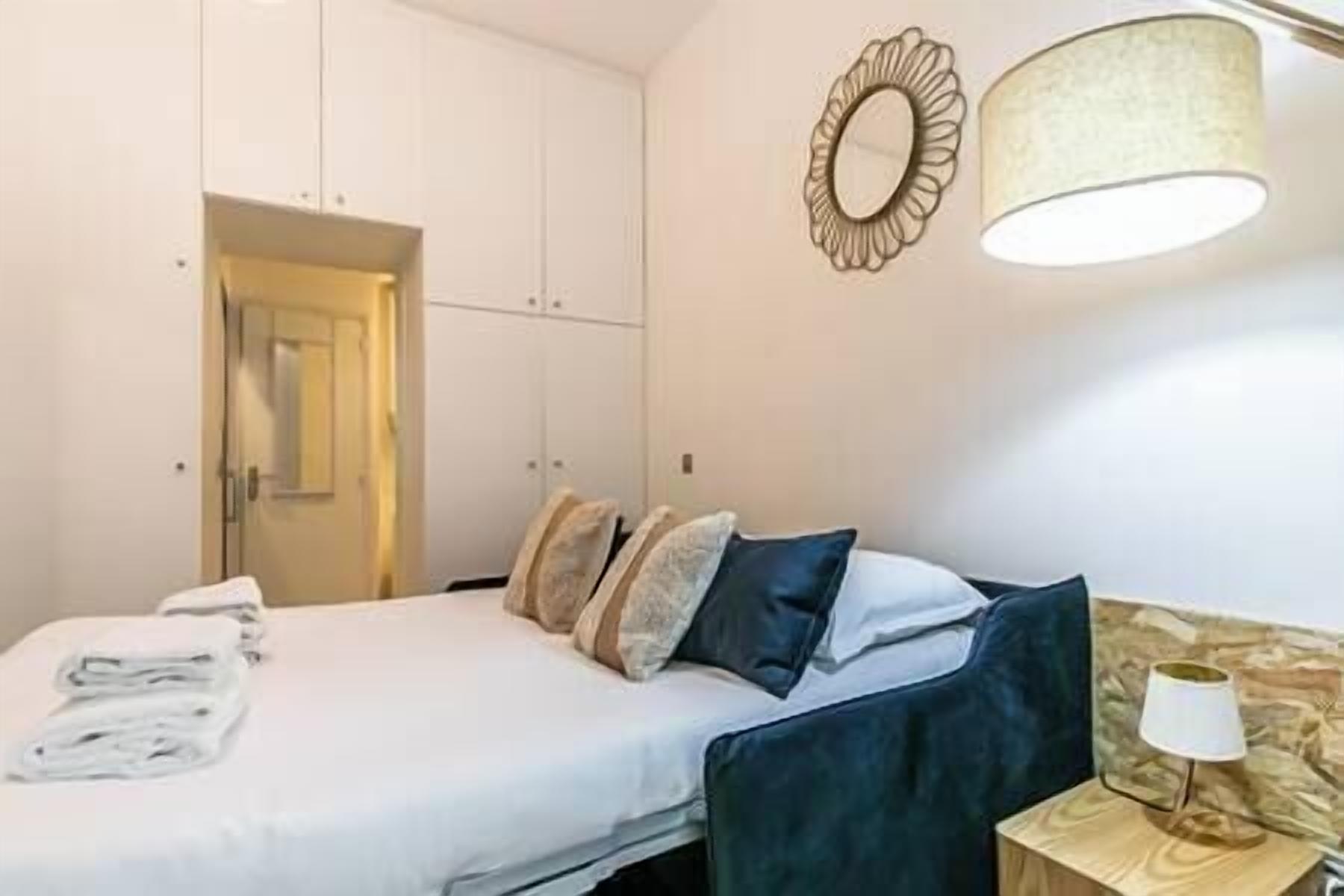 Een net opgemaakt bed met kussens, een bedlampje en een spiegel aan de muur.