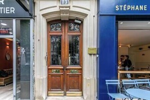 Una puerta doble de madera con paneles de vidrio, el número '13' arriba y un escaparate azul donde se ve 'STÉPHANE'.