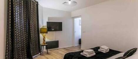 A bedroom with a bed, a TV mounted on the wall, and a door leading to another room.