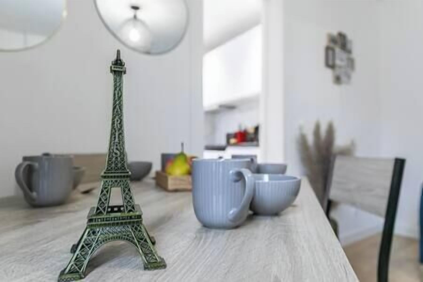 Un tavolo da pranzo con una riproduzione della Torre Eiffel, tazze grigie e una ciotola di frutta.