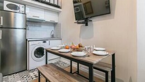 A compact kitchen with a built-in washing machine, a stainless steel refrigerator, and a dining table set with plates and bowls. - Splendid 8-room apartment near Bercy (Paris)