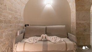 Una habitación acogedora con pared de piedra, una cama con dos almohadas y una lámpara sobre ella.
