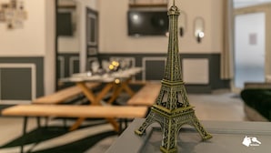 Una maqueta de la Torre Eiffel en una habitación moderna con una mesa de comedor y sillas, un televisor en la pared y un estante pequeño.
