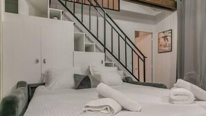 Un dormitorio con cama, almohadas, una toalla doblada, una escalera y un estante en la pared.