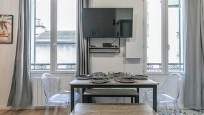 Un comedor con una mesa dispuesta para cuatro personas, un televisor montado encima y un balcón visible a través de las ventanas.