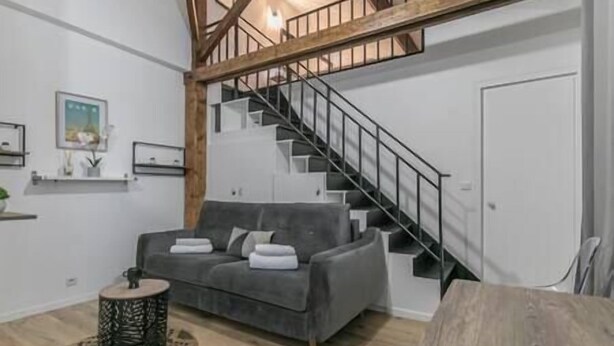Una sala moderna con un sofá gris, una mesa de centro de madera y una escalera con barandilla de metal.